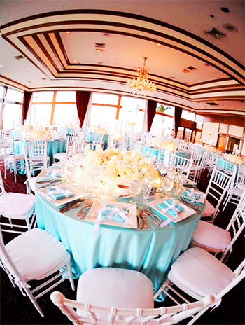 wedding reception tables with Tiffancy blue tablecloths, white Chiavari chairs with white cushions, and large square white chargers with Tiffany gifts tied with white bows, and white rose centerpieces
